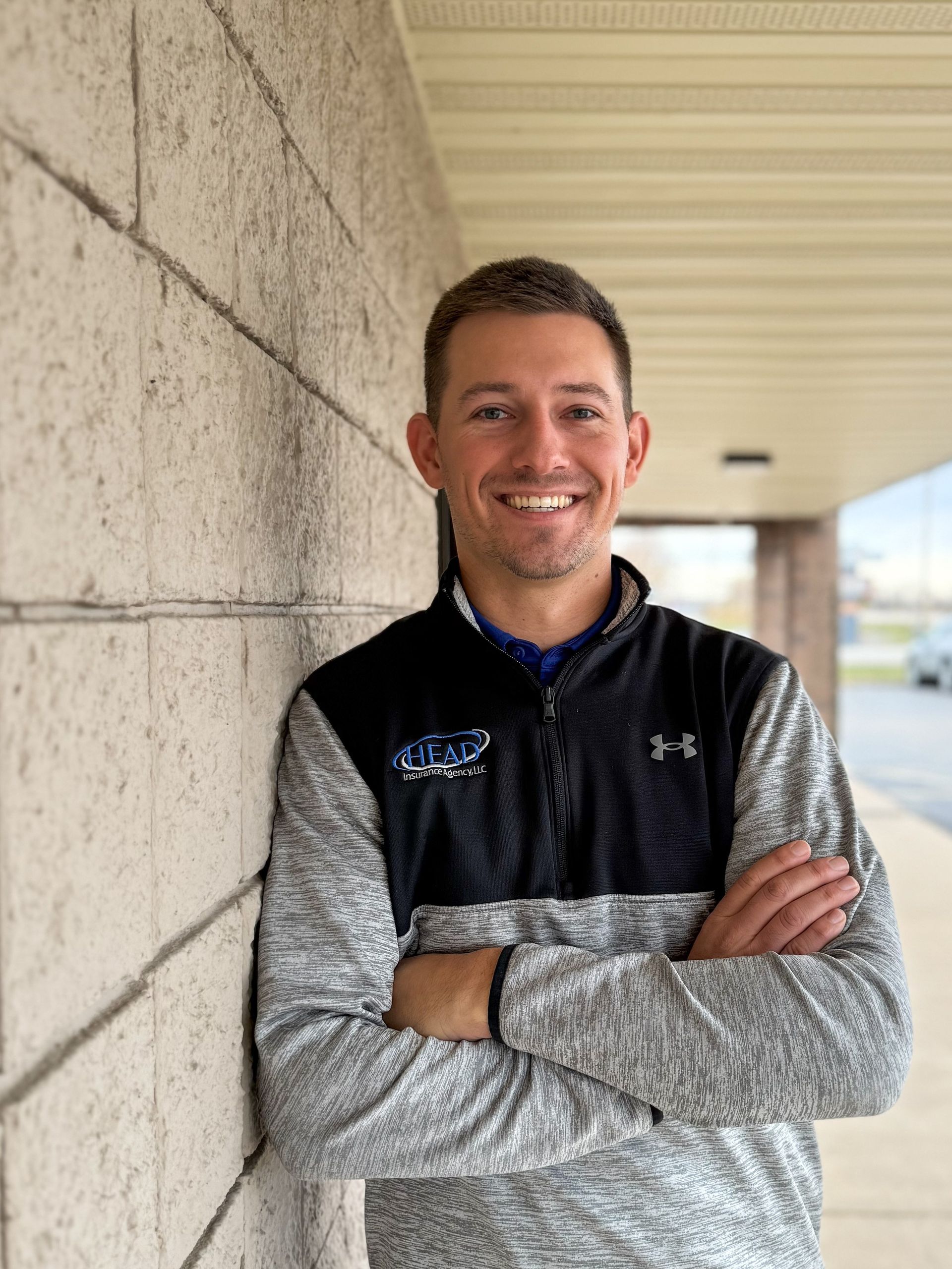 Man in gray polo shirt smiles, standing in front of a textured wall.