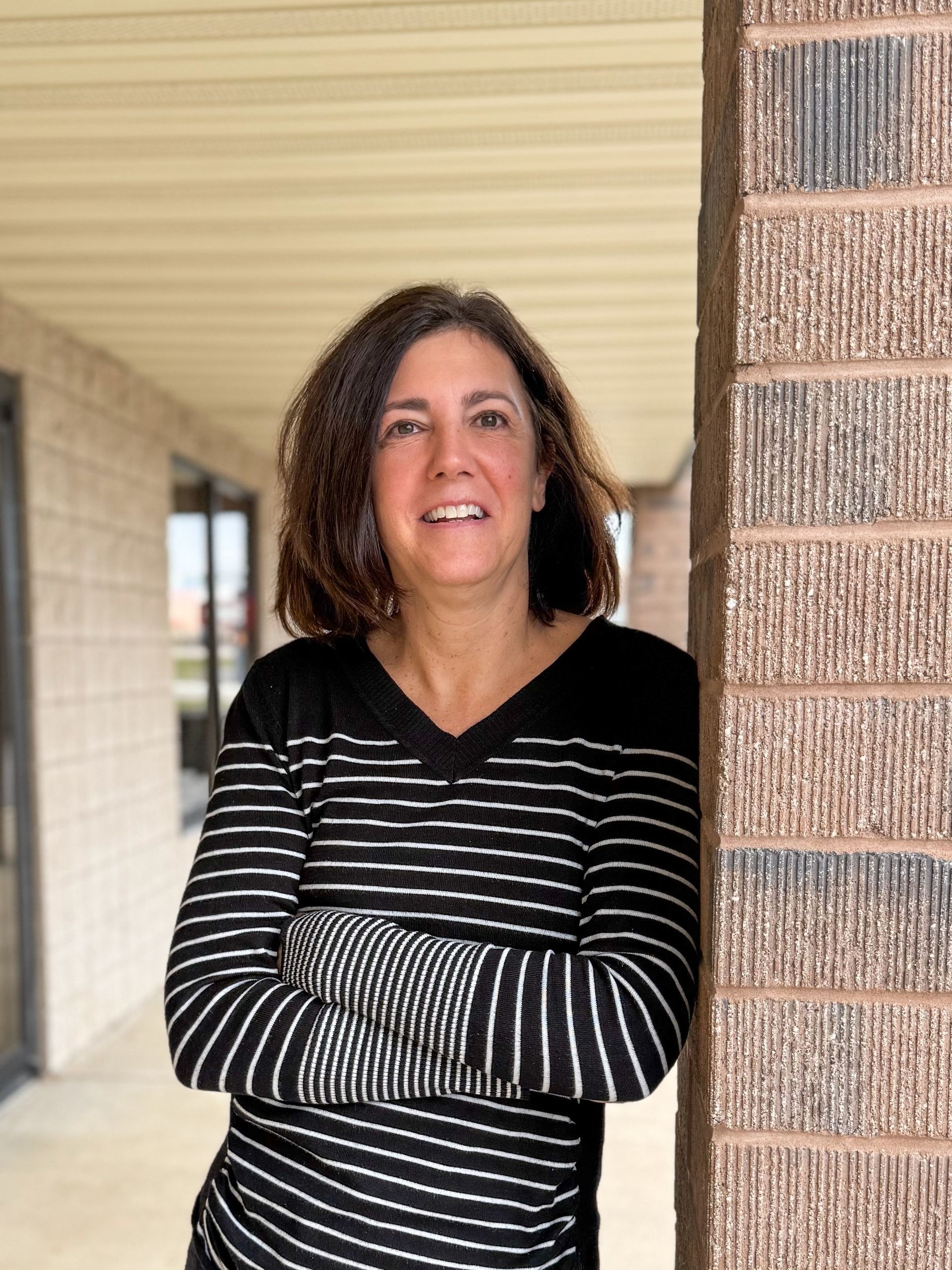 Woman in blue shirt with arms crossed, smiling in front of a textured wall.