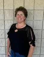 Woman smiling, leaning against a textured wall, wearing a black top and jeans.