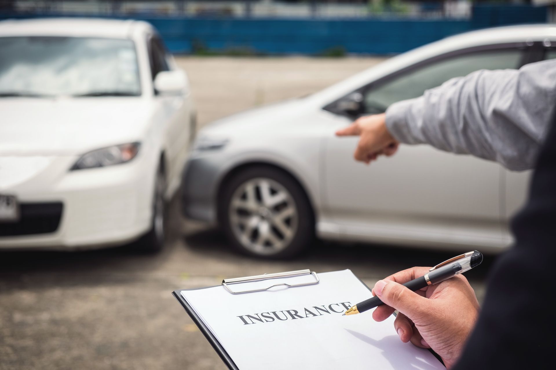 Person pointing at car damage, holding an insurance form, after a car accident.
