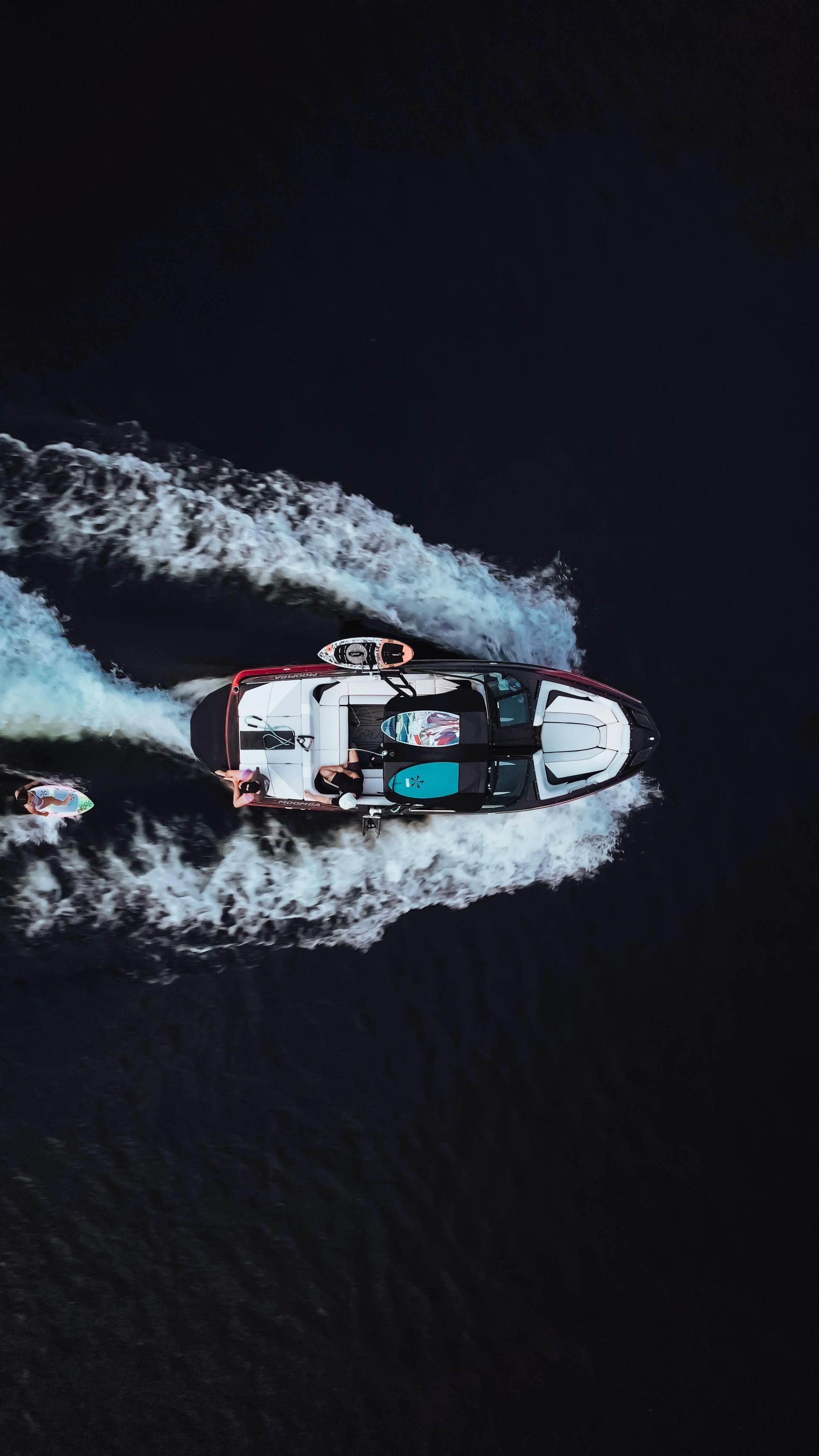 Boat on dark water, creating white wake. People onboard, pulling someone on a wakeboard.