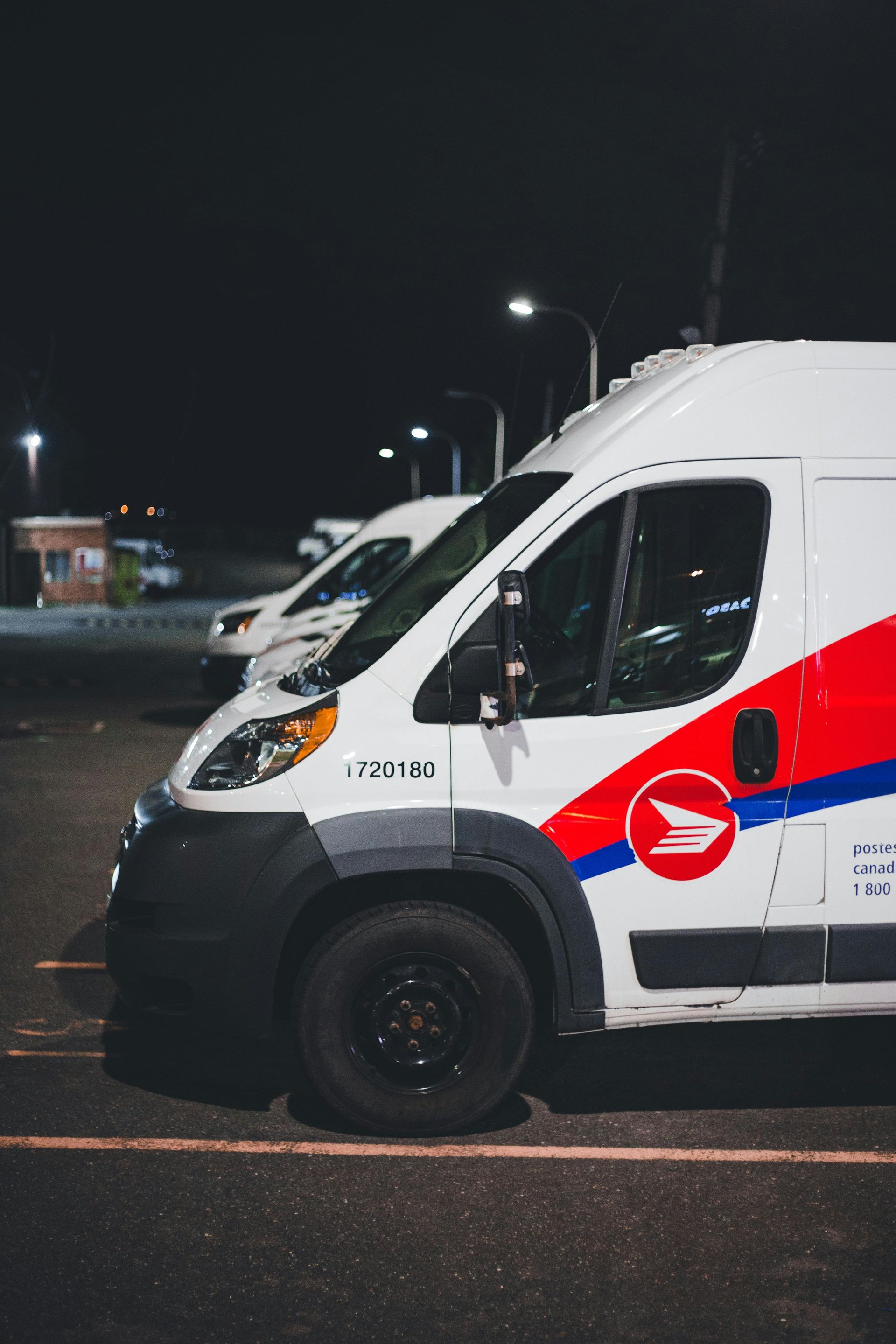 USPS delivery vans parked at night, red, white, and blue branding, under streetlights.