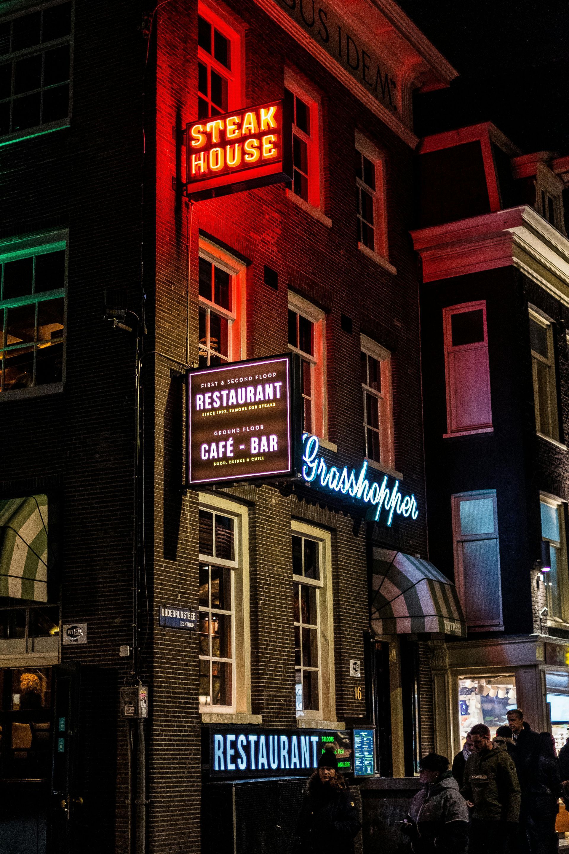 Steak House restaurant with neon signs at night. Brick building with a few people visible near the entrance.