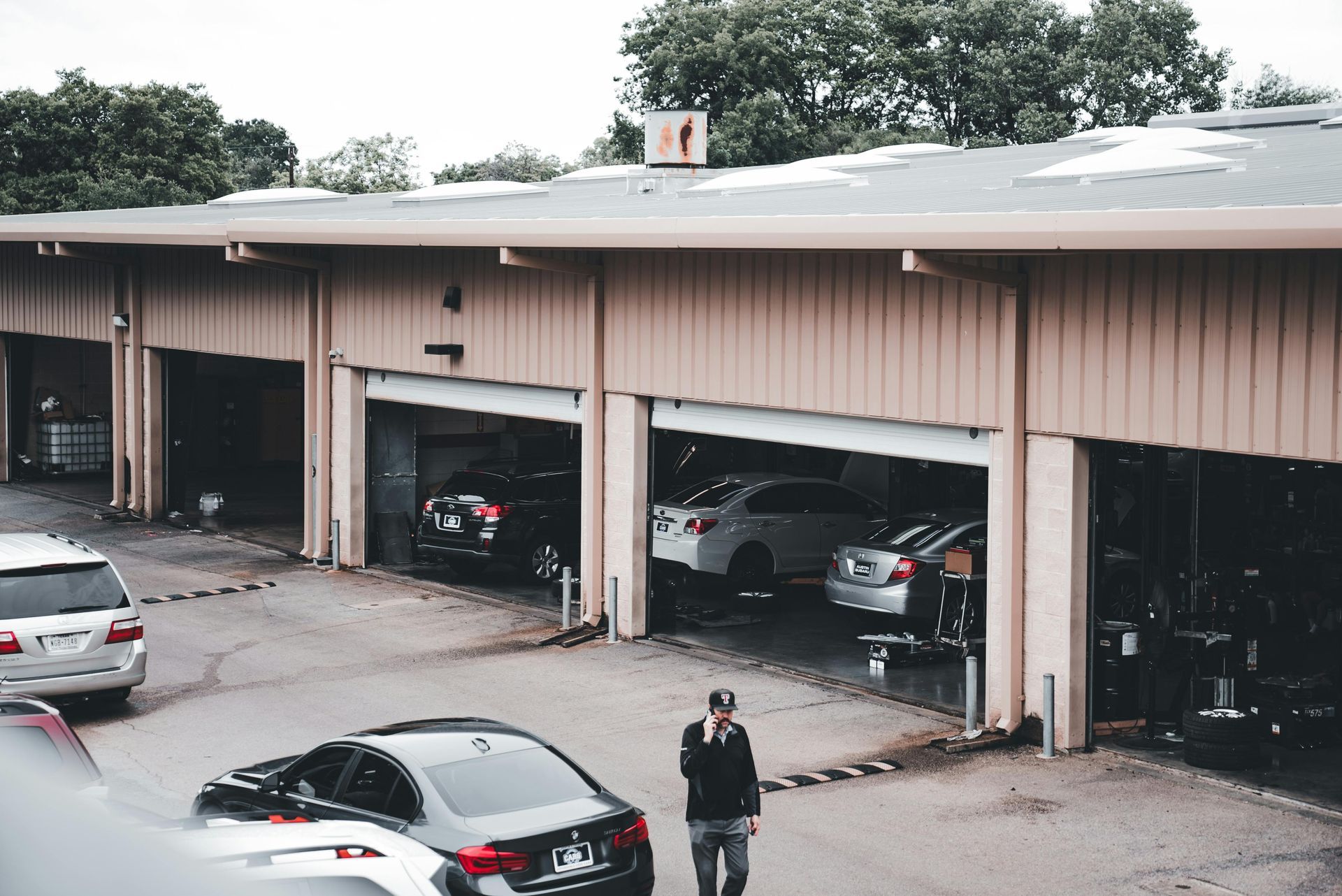 Cars parked in open garage bays of a tan-colored building; a man in a hat stands in front.