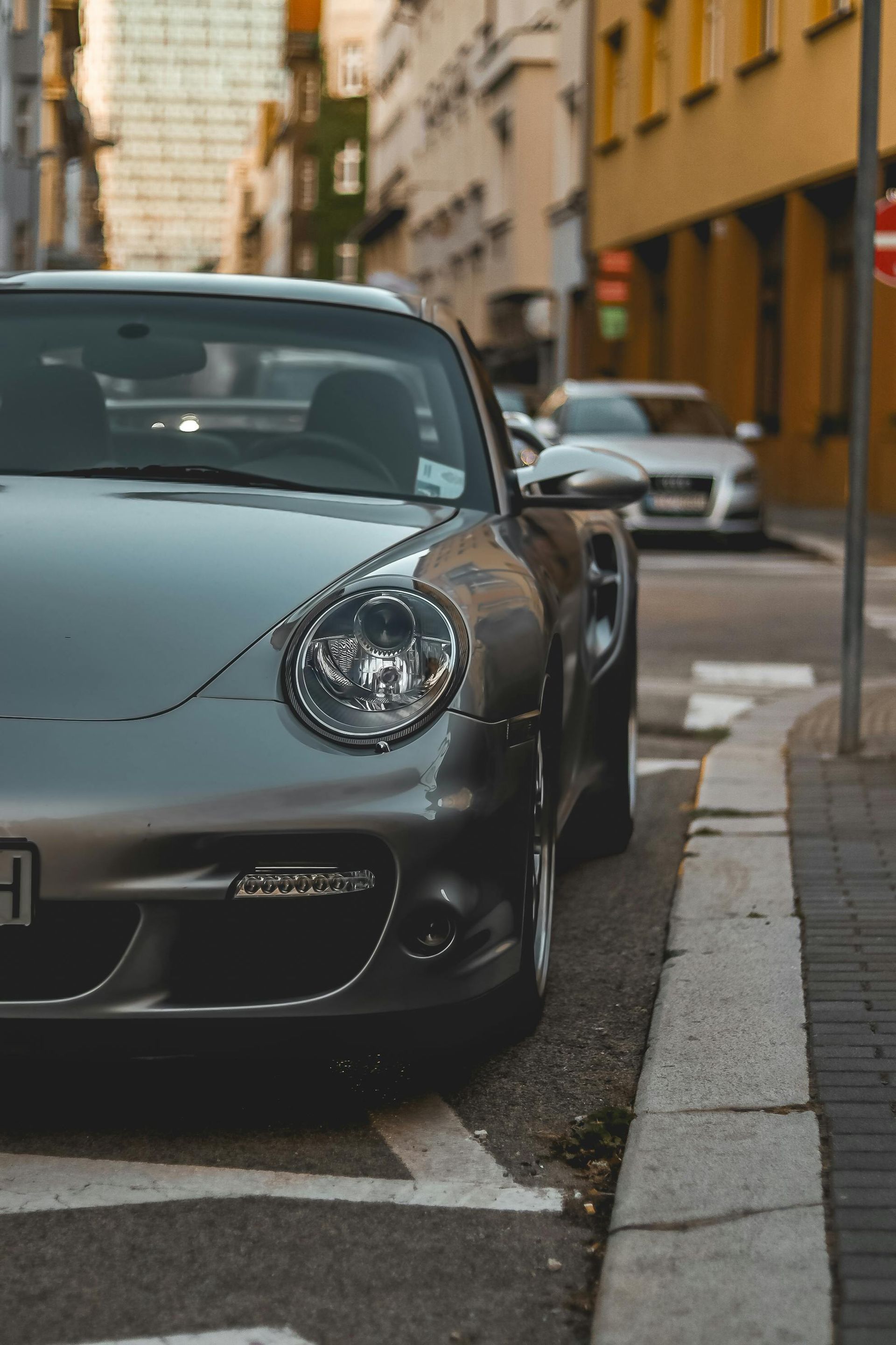 Silver Porsche parked on a city street next to a curb, with an Audi in the background.