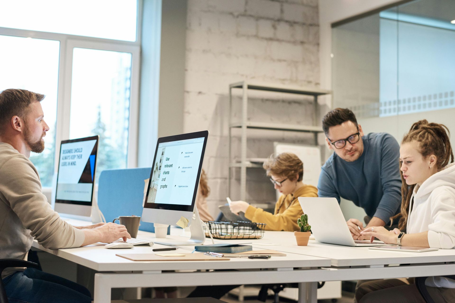 Office workspace: People collaborating at computers, one is assisting a colleague.