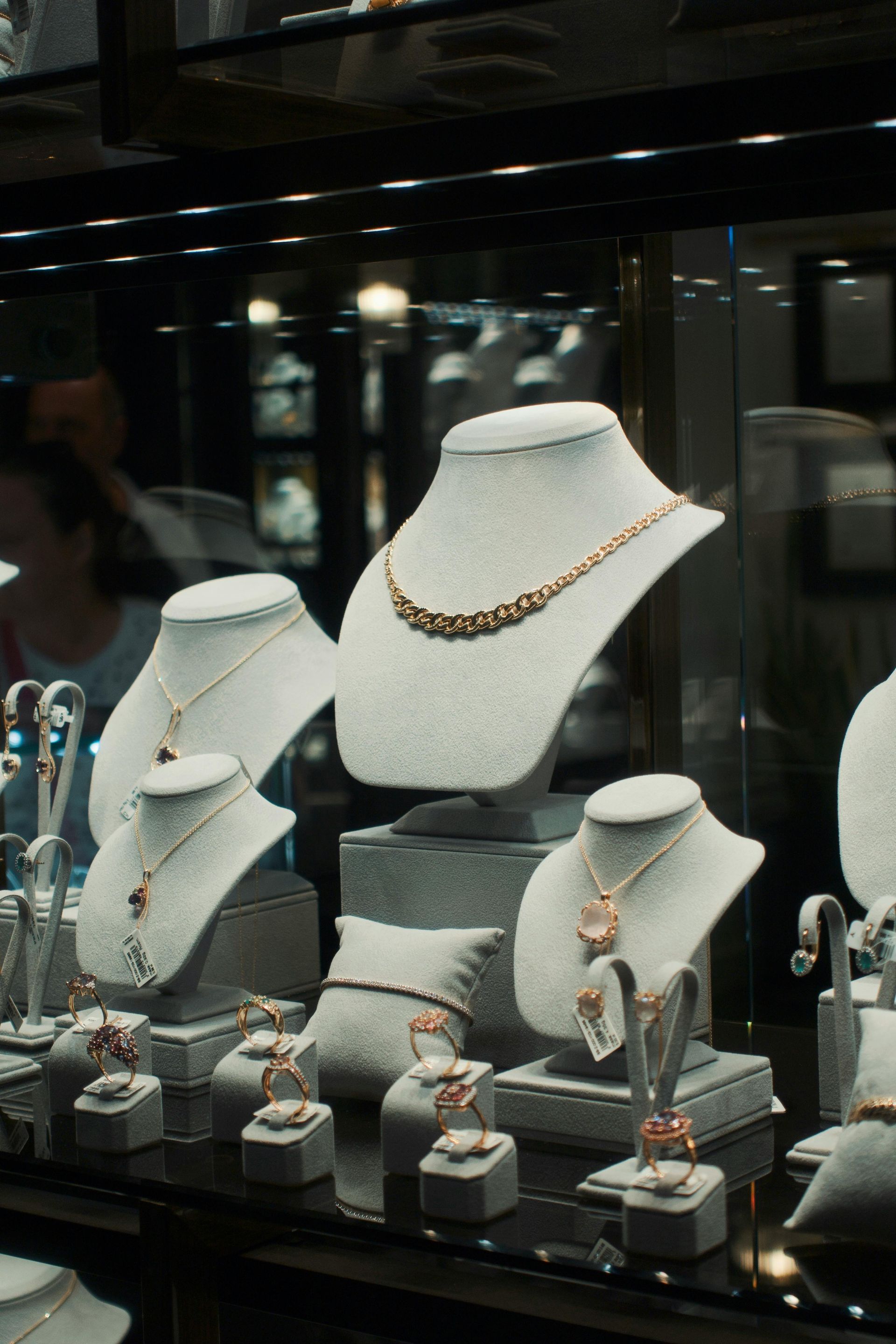 Jewelry display case featuring necklaces, bracelets, and rings on white busts in a shop.
