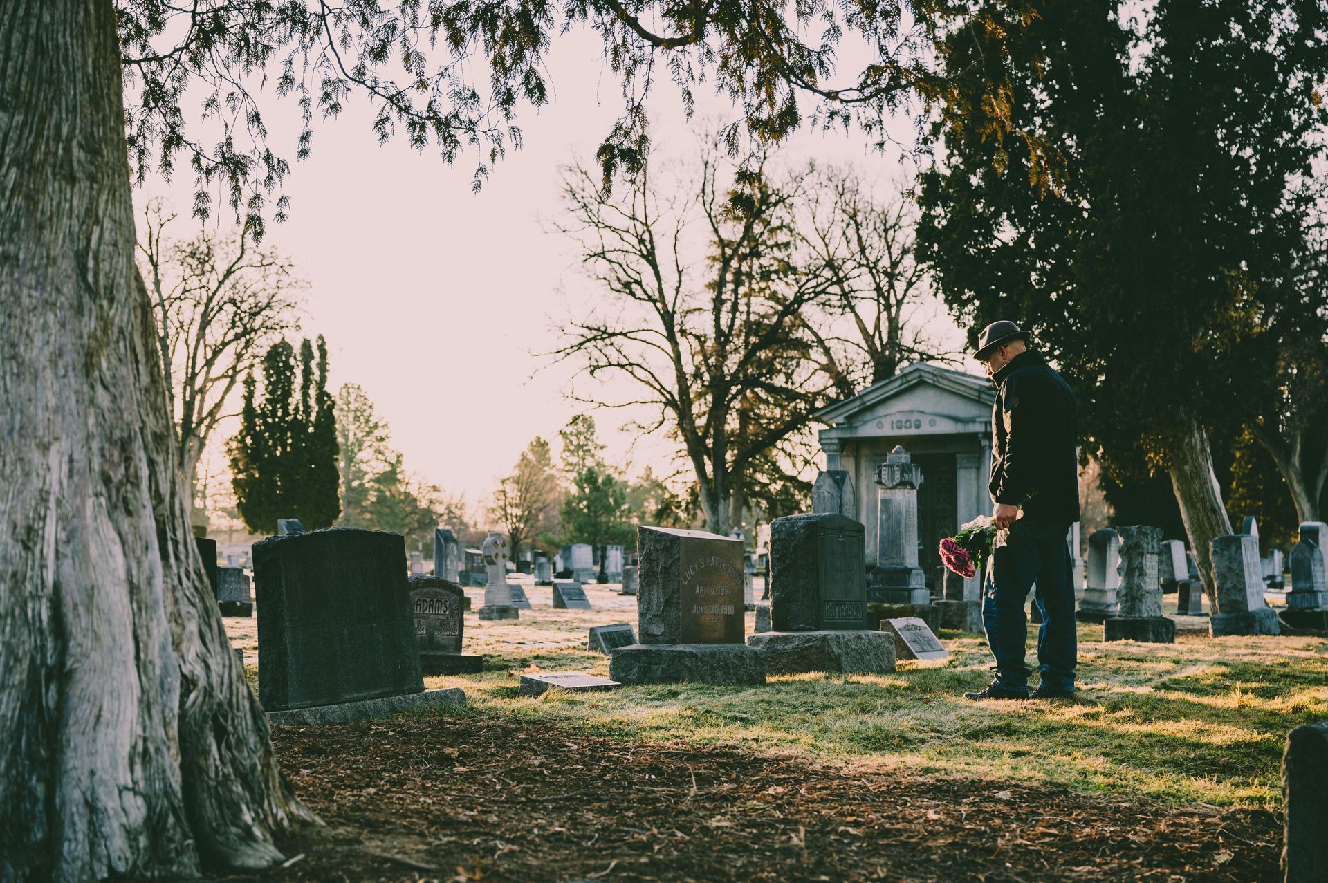 People in black attire at a funeral, some with their heads bowed, a man comforts a woman.