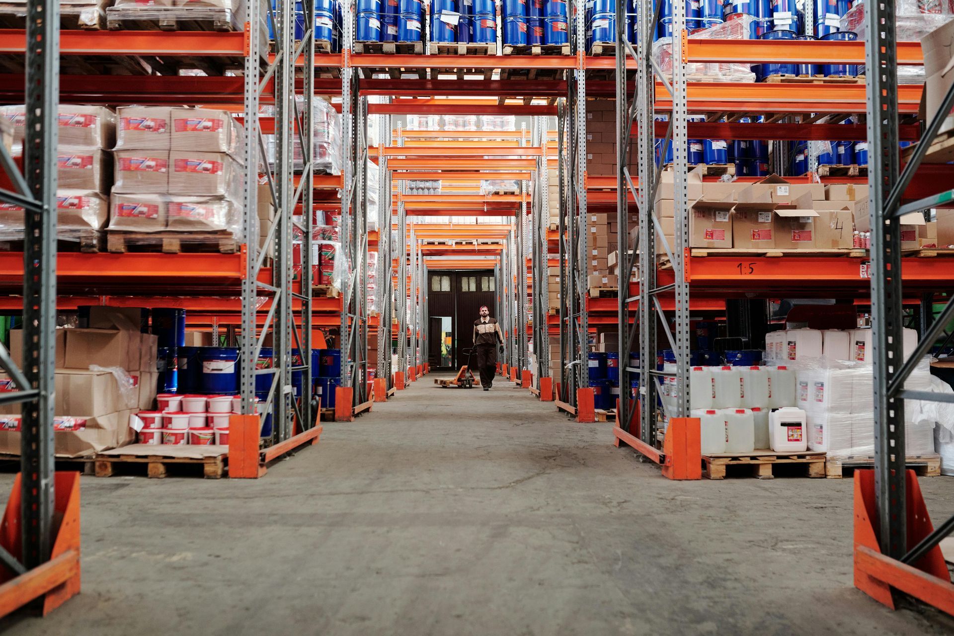 Warehouse interior with stacked shelves, person walking down aisle.