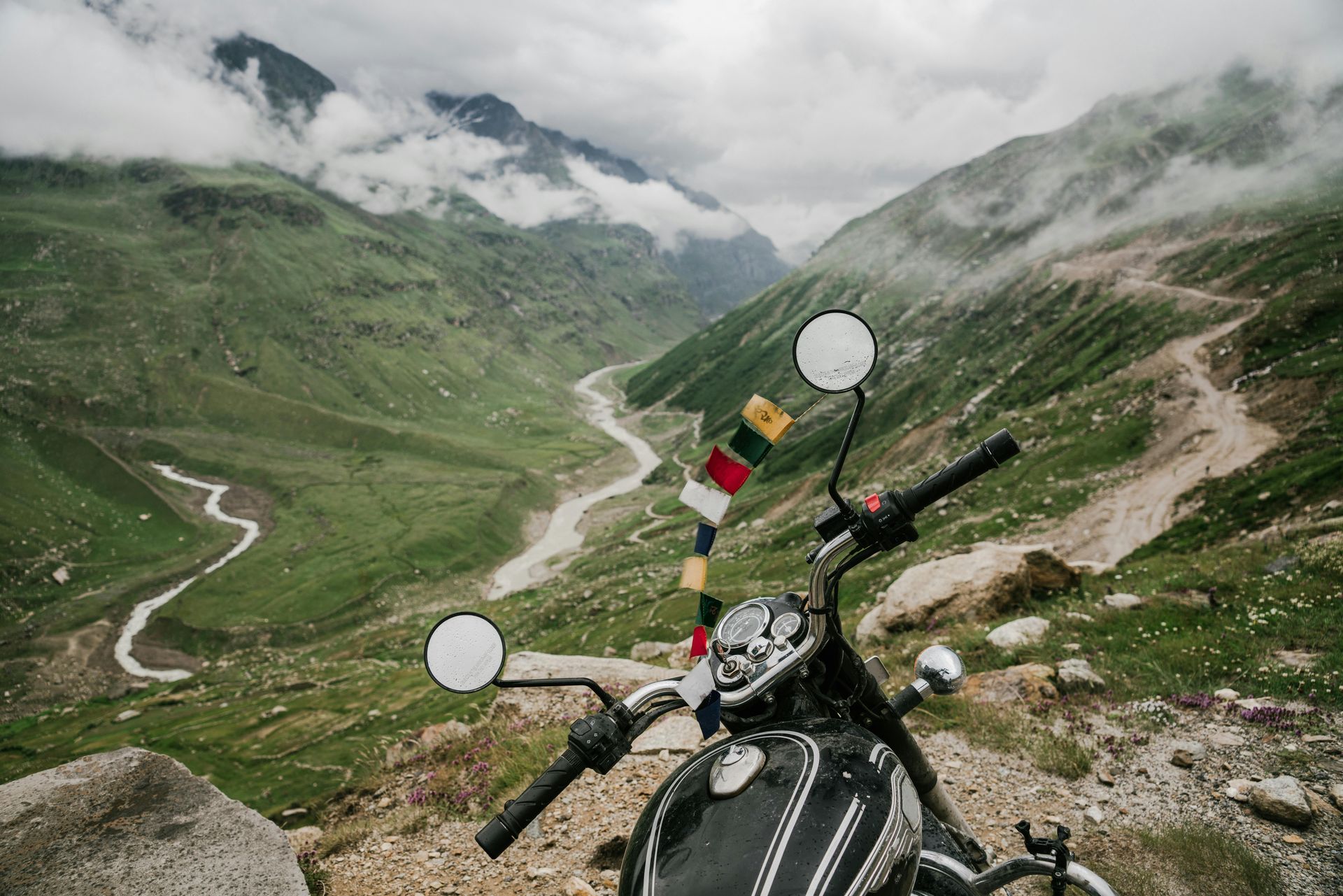 Motorcycle parked on a mountain road, overlooking a green valley with a winding river.