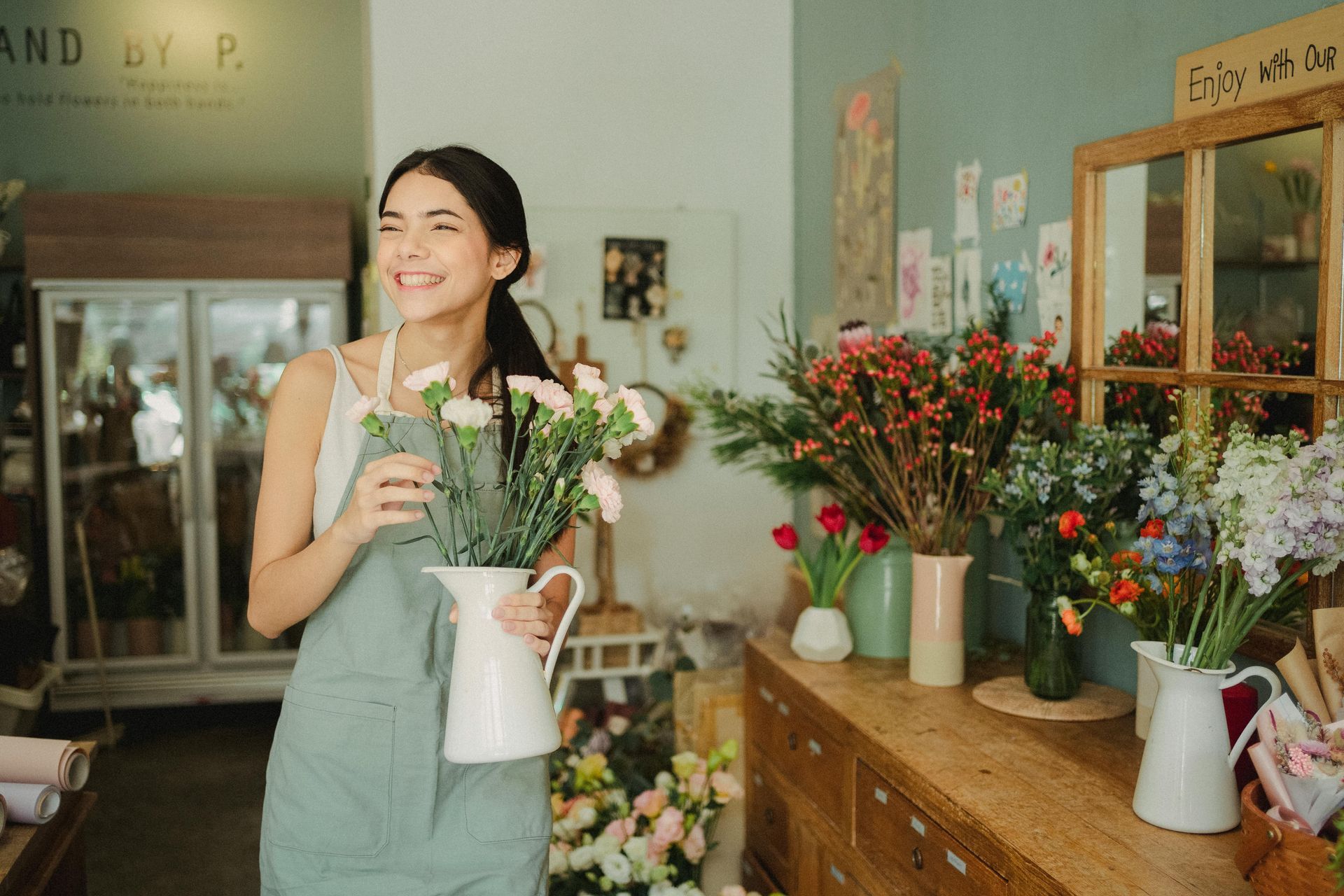 Smiling florist holding flowers in a jug, standing in her shop.