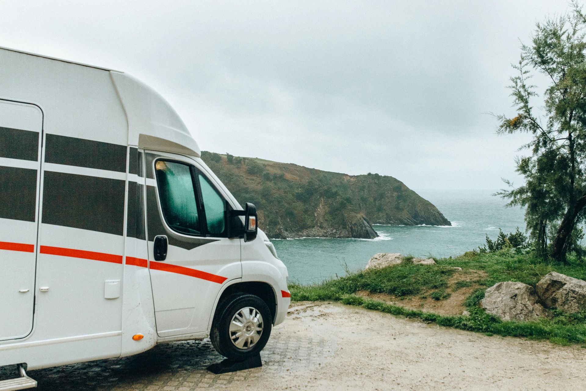 White RV parked near a rocky coastline under an overcast sky.