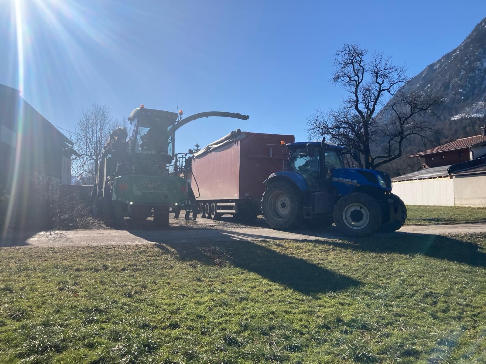 Ein Traktor lädt Heu in einen roten Anhänger.