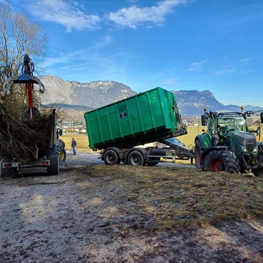 Ein grüner Müllcontainer wird von einem Traktor auf einen Anhänger geladen.