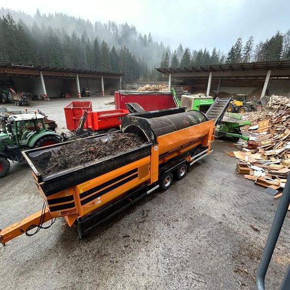 Ein großer orangefarbener Lastwagen steht auf einem Parkplatz neben einem Holzstapel.