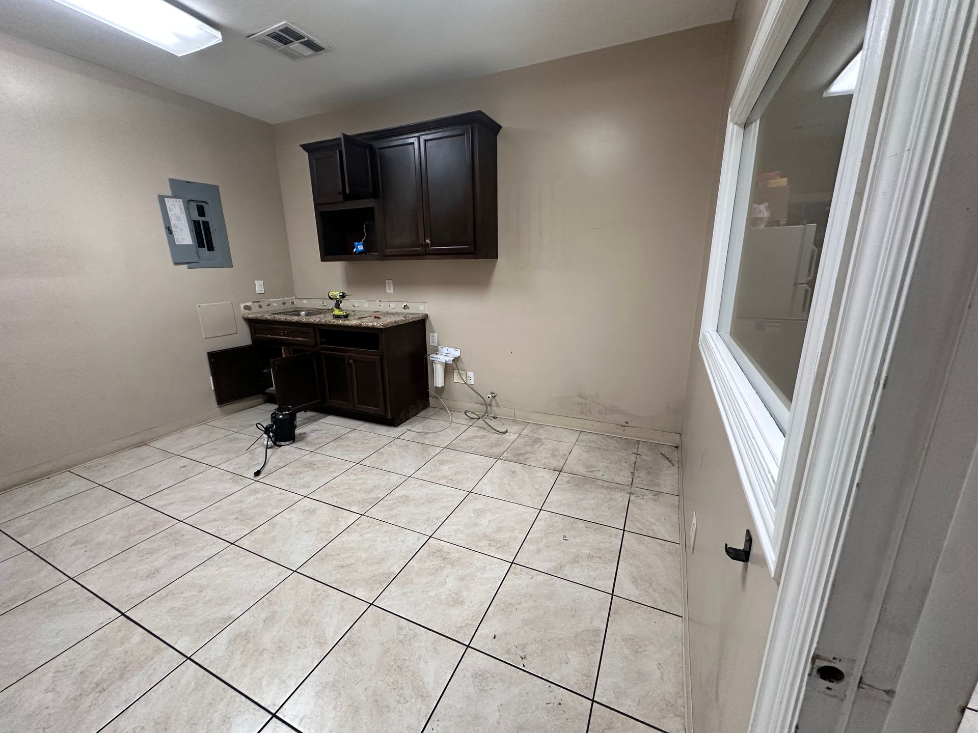 Small room with dark cabinets, a sink, and tiled floor. A window is on the right.