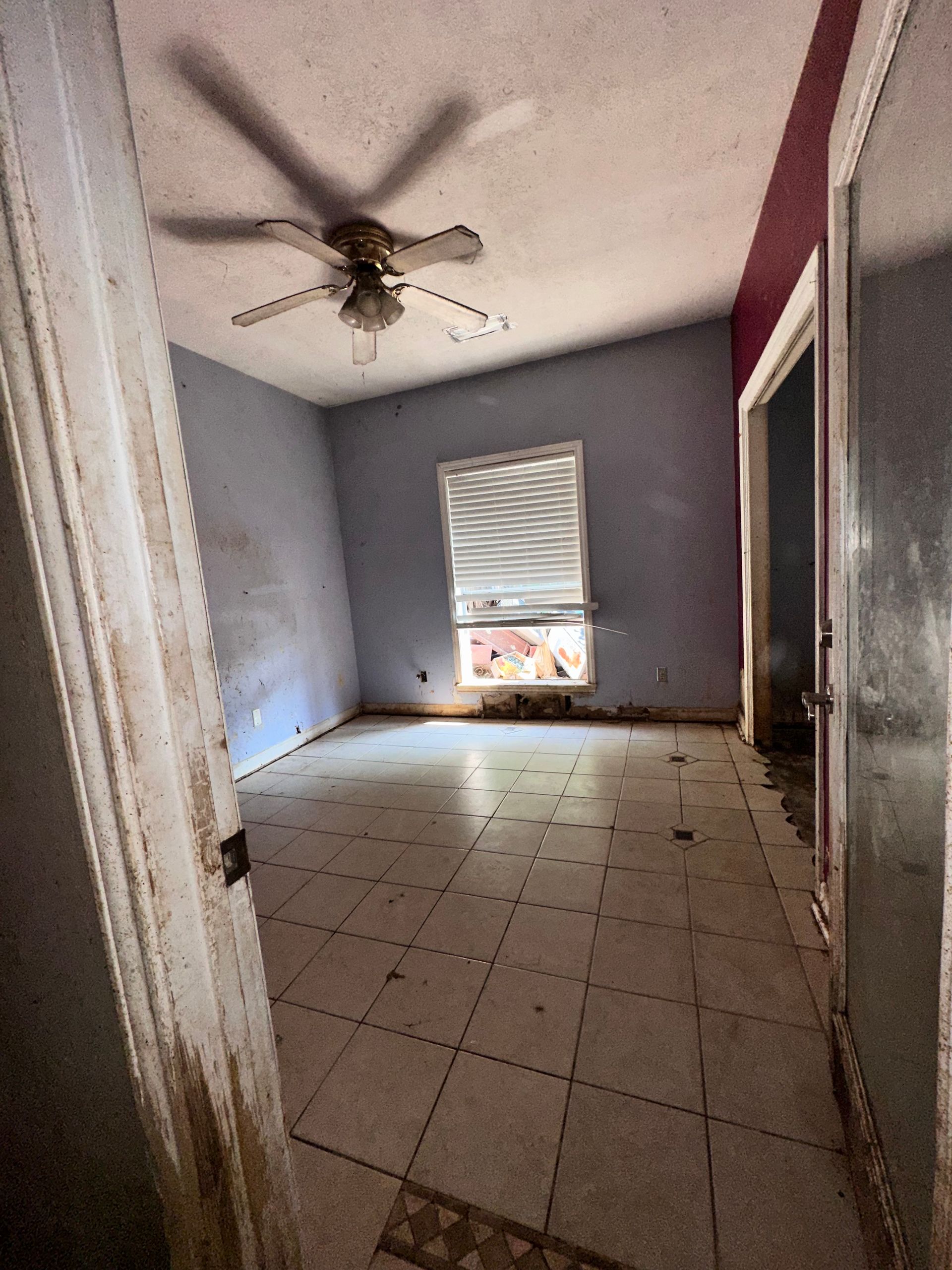 Empty room with tile floor, blue walls, a window, ceiling fan, and open doorway.