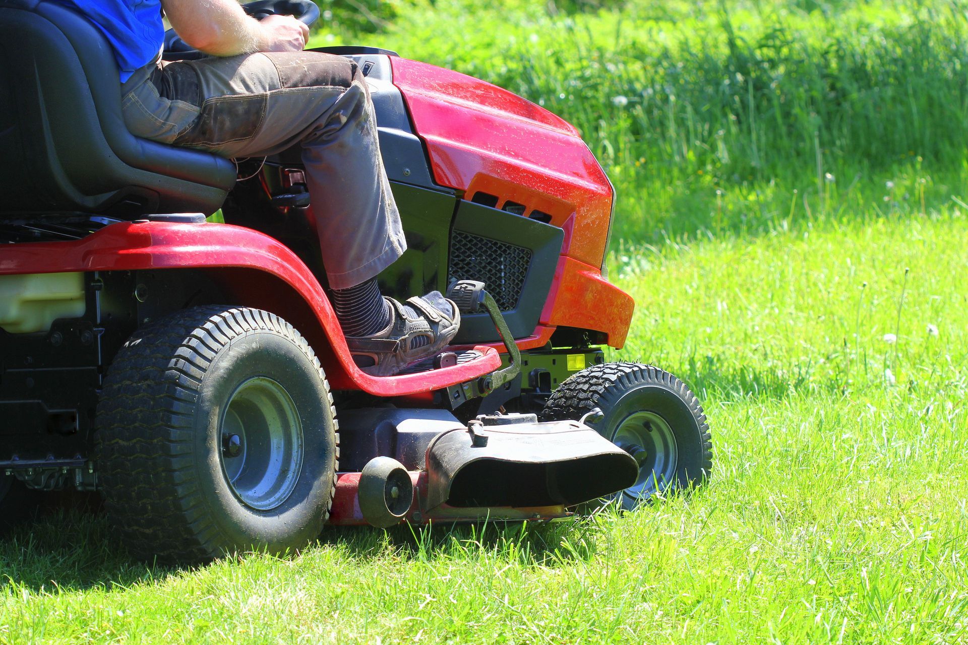 Gardener driving a riding lawn mower in a garden.