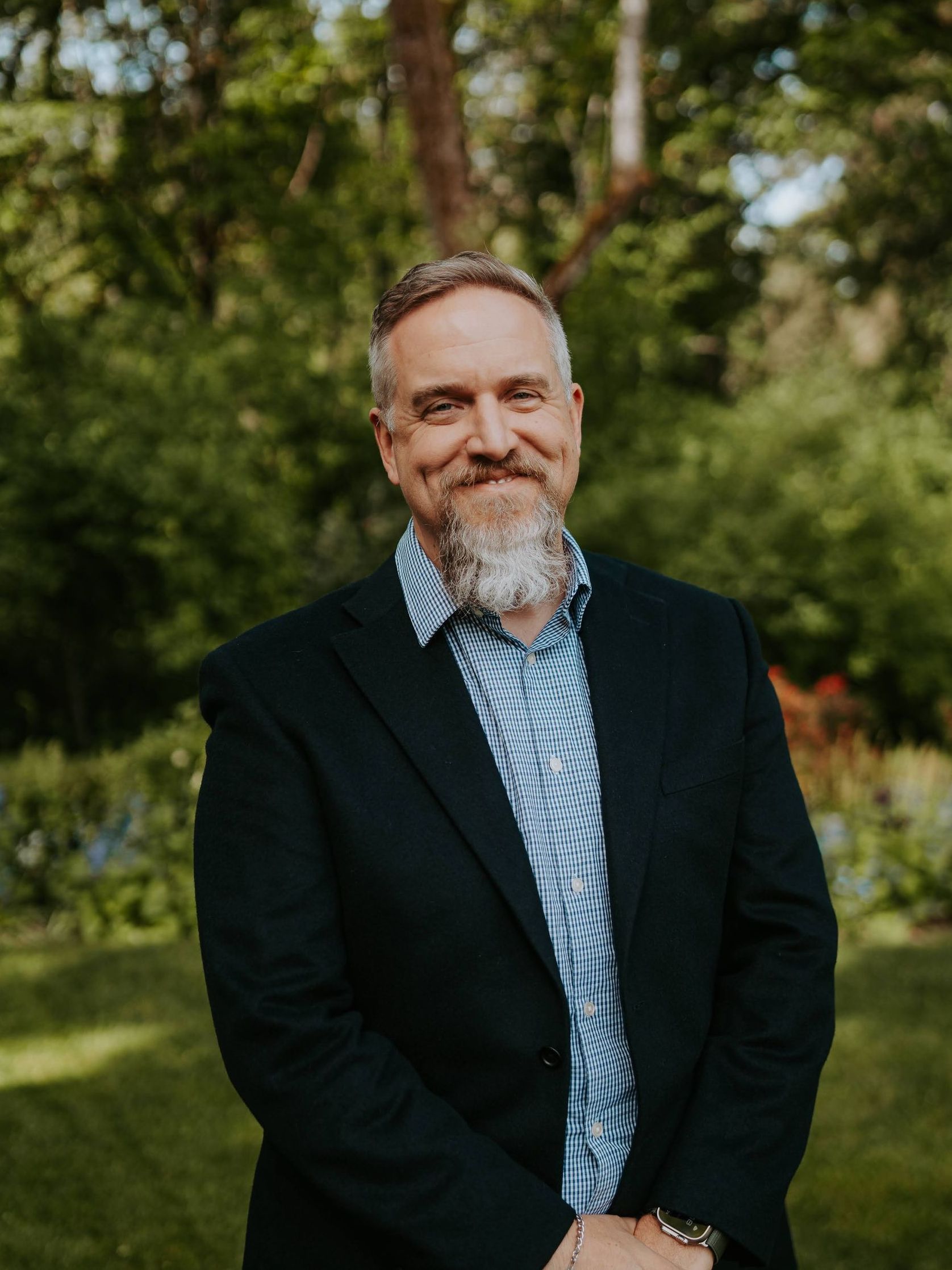 A man in a suit and striped shirt is standing in front of a forest.