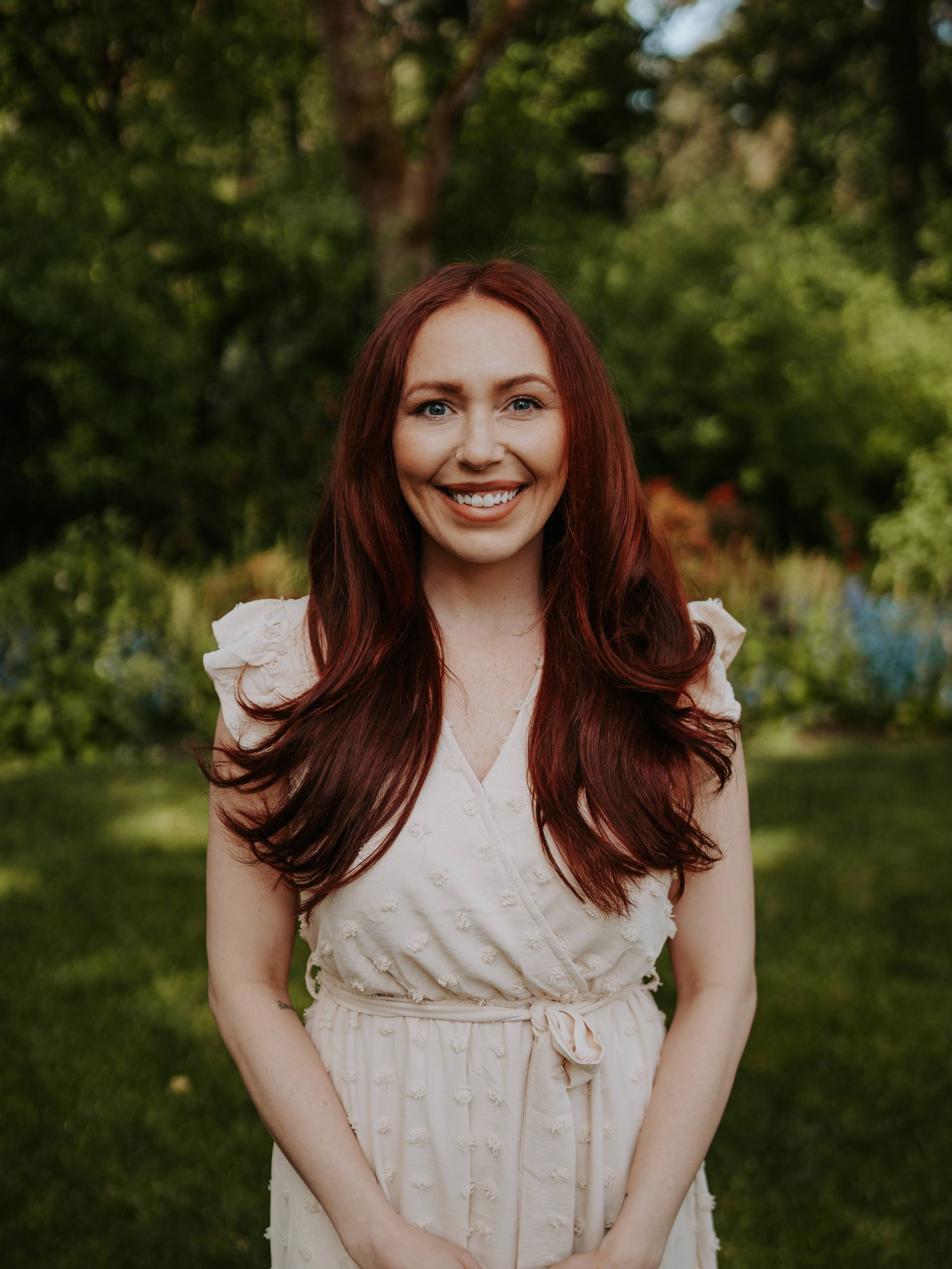 A woman with long red hair is wearing a white dress and smiling.