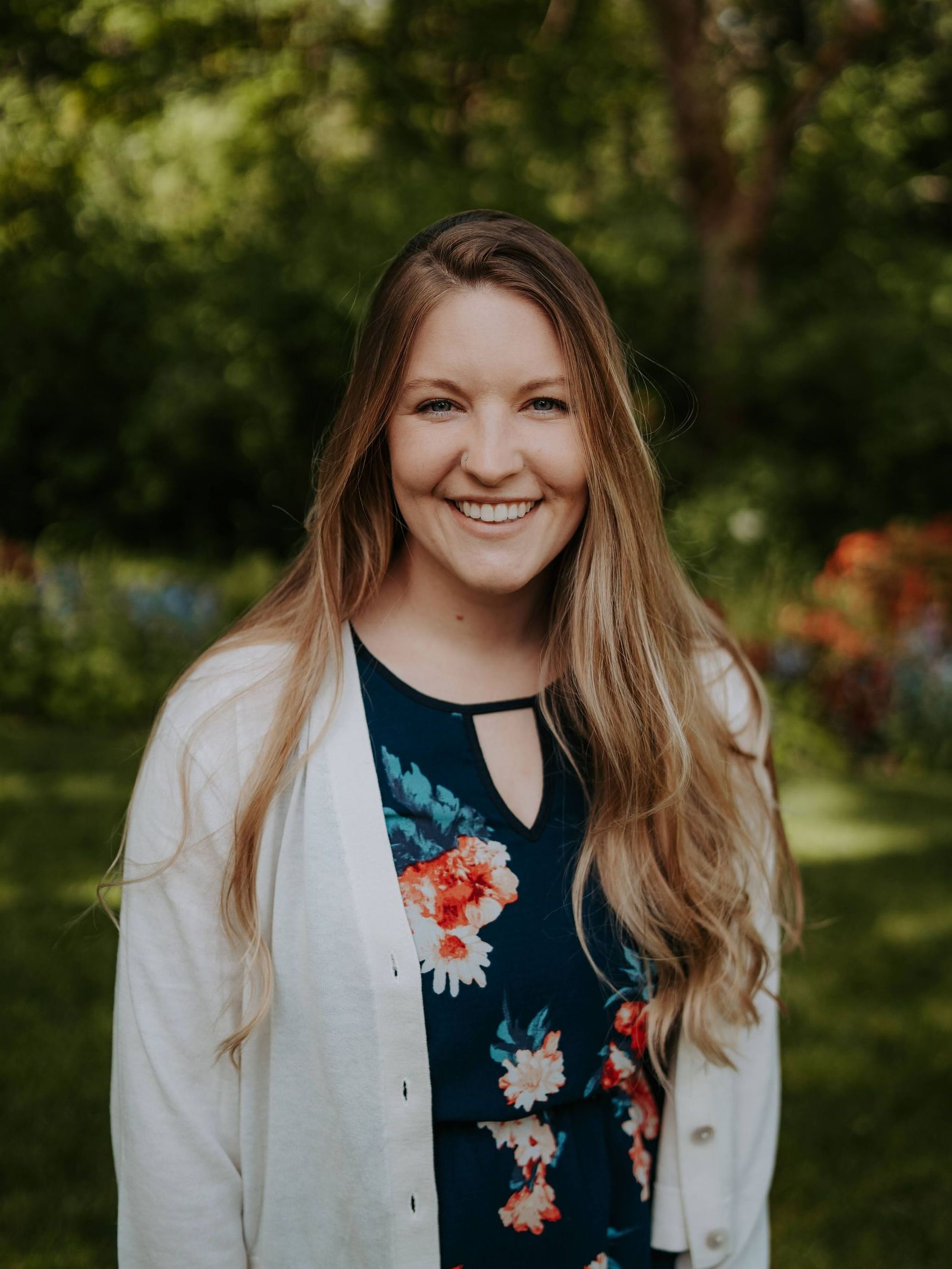 A woman in a floral dress and white cardigan is smiling for the camera.