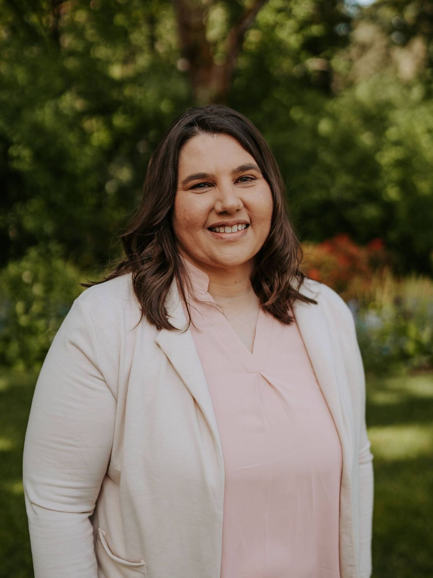 A woman in a pink shirt and white cardigan is smiling for the camera.