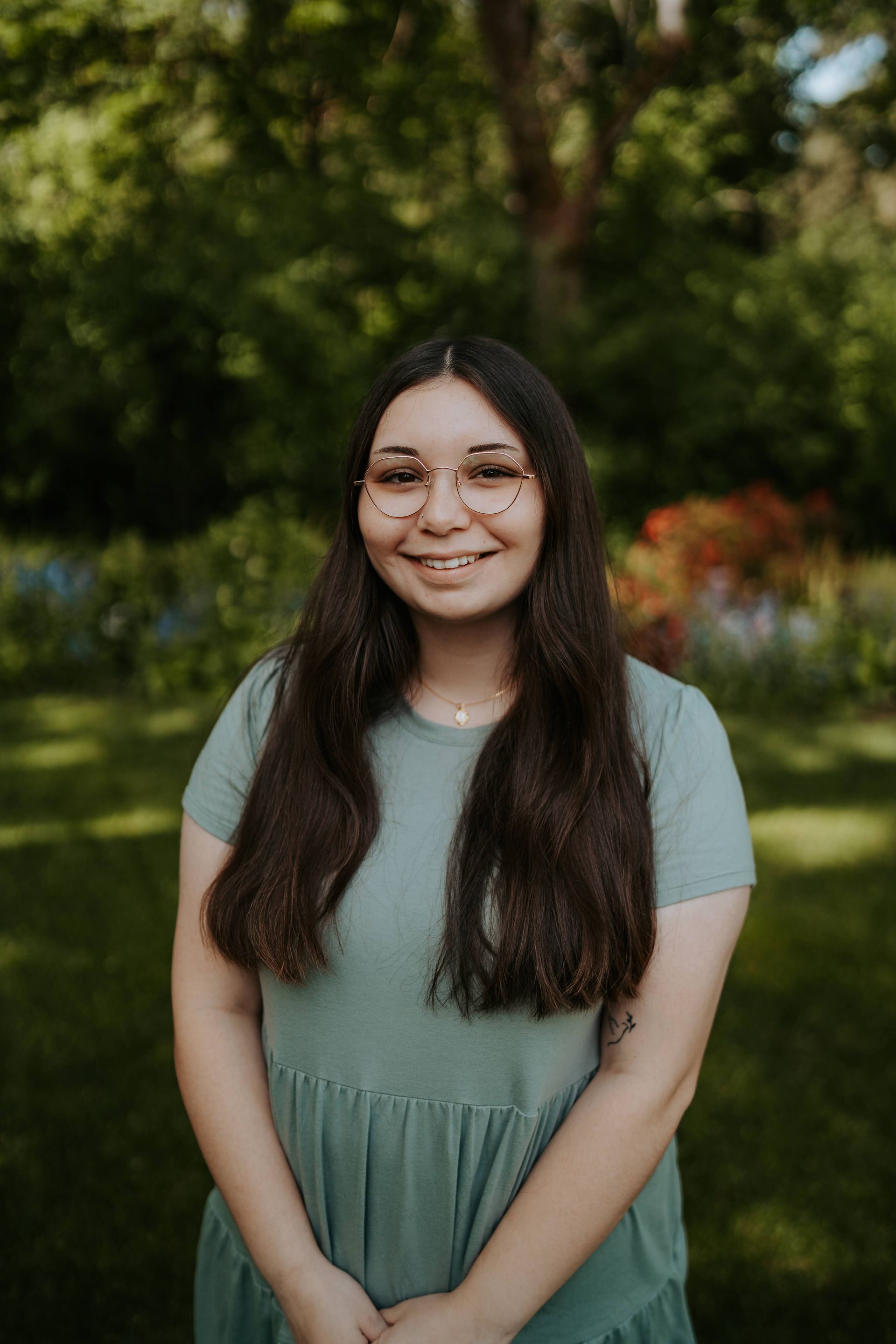 A young woman wearing glasses and a green dress is standing in the grass.