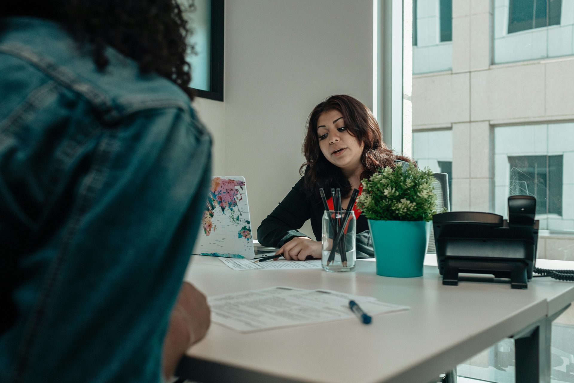 Woman in office speaks to another person, near a desk, papers.