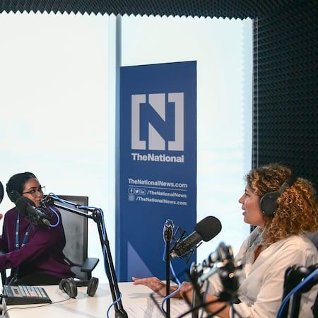 Two women are talking into microphones in front of a sign that says the national