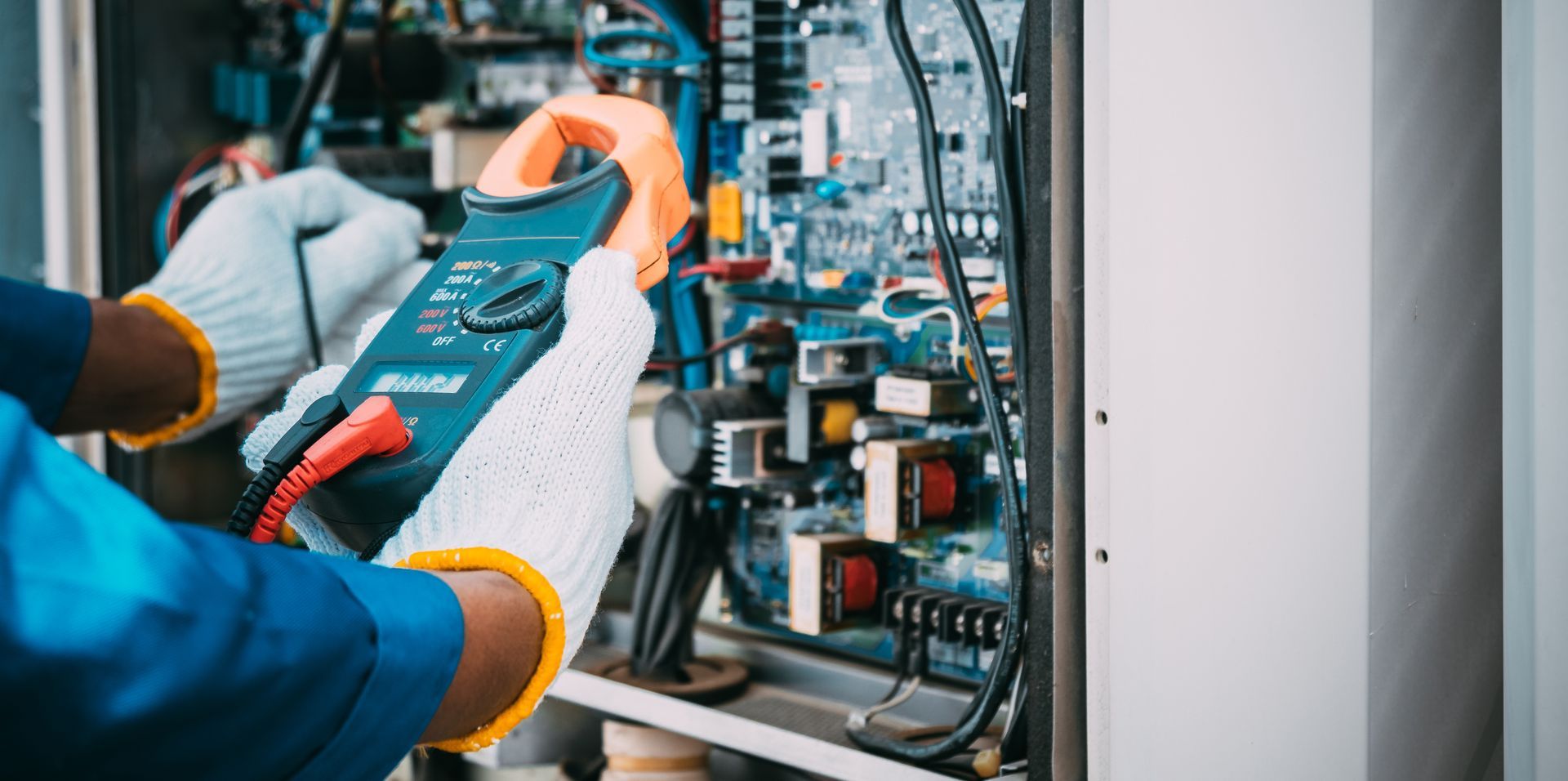An electrician is working on a machine with a clamp meter.