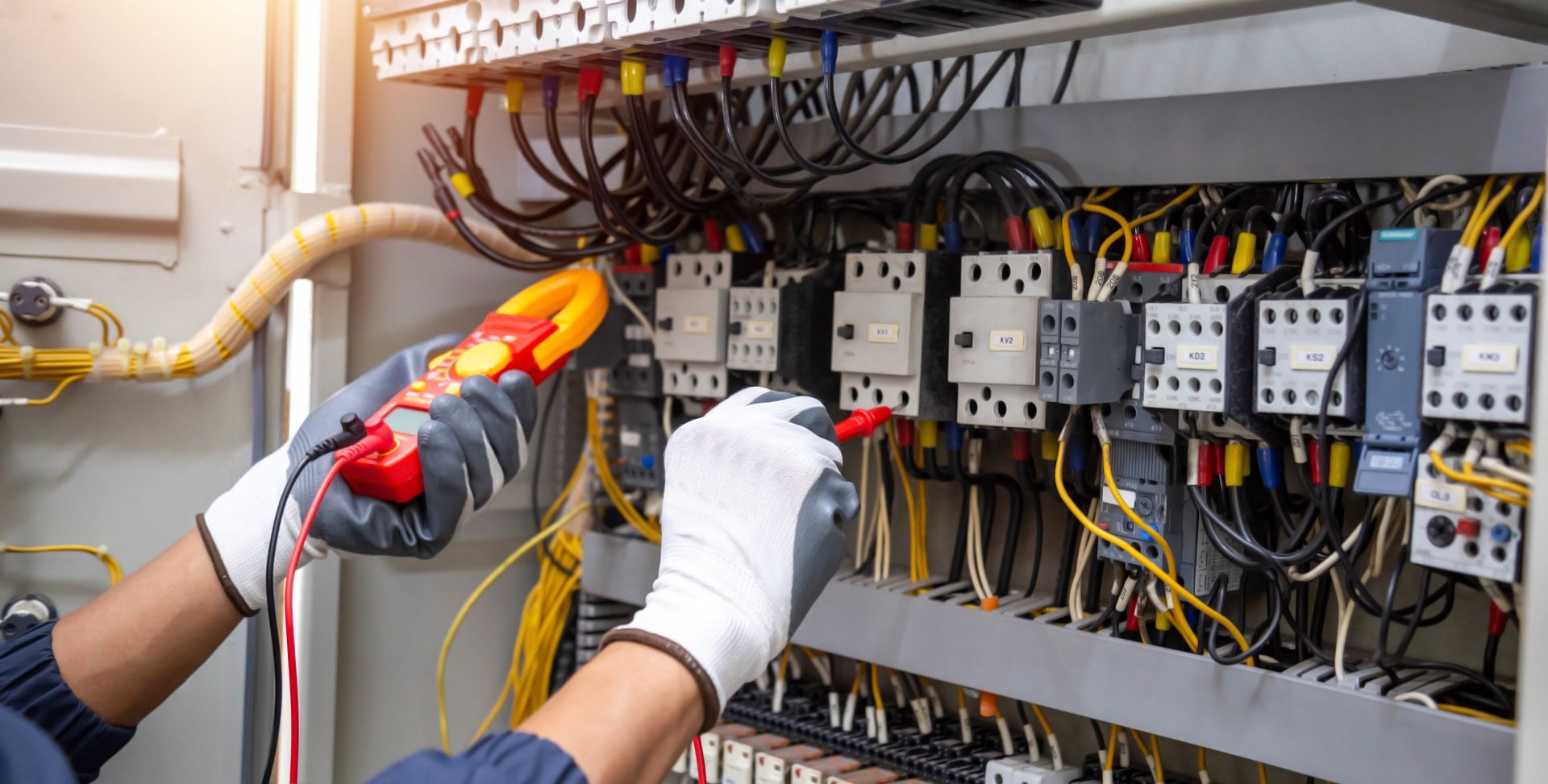 An electrician is working on an electrical panel with a multimeter.