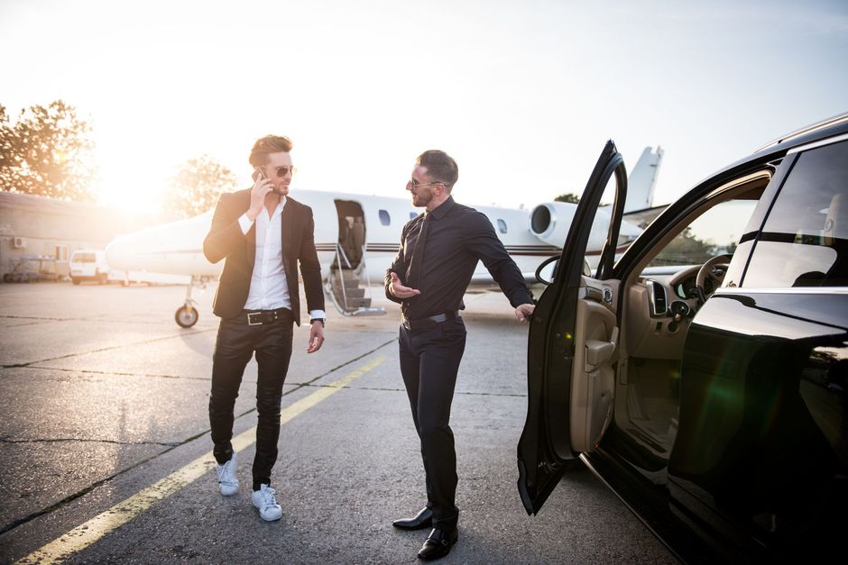 Two men are standing next to a car and a plane.