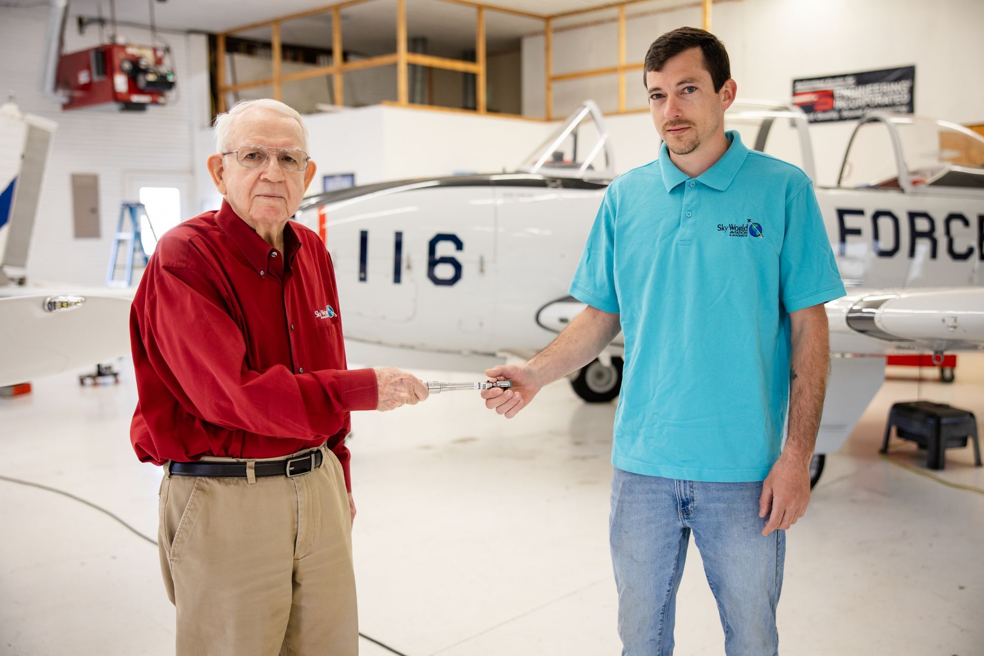 Person in a maroon hoodie inspecting a red-and-white small airplane in a hangar.