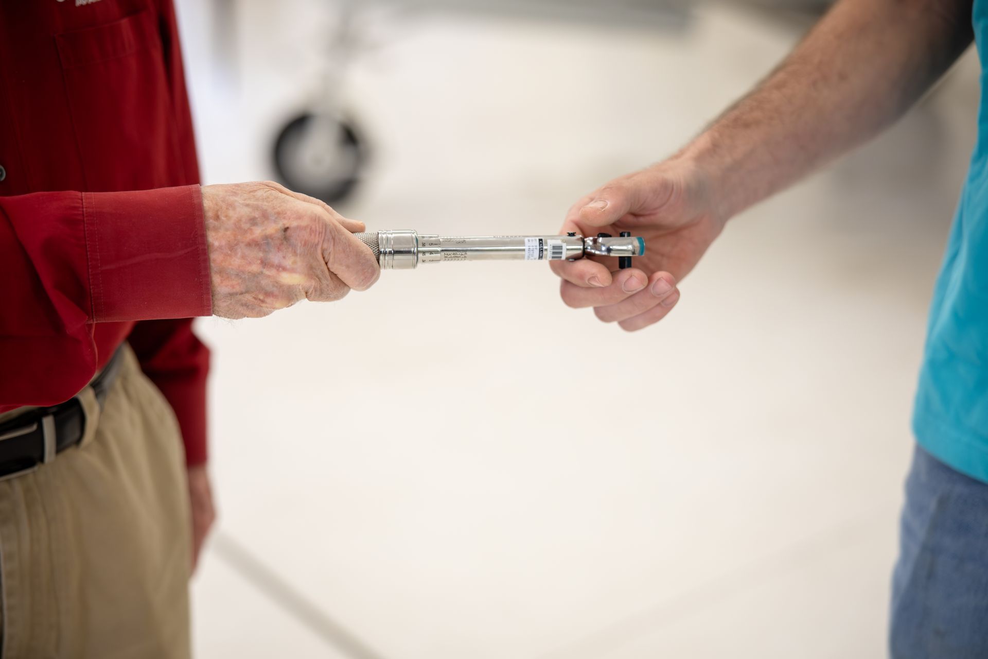 Two people exchanging a silver flute against a blurred indoor background