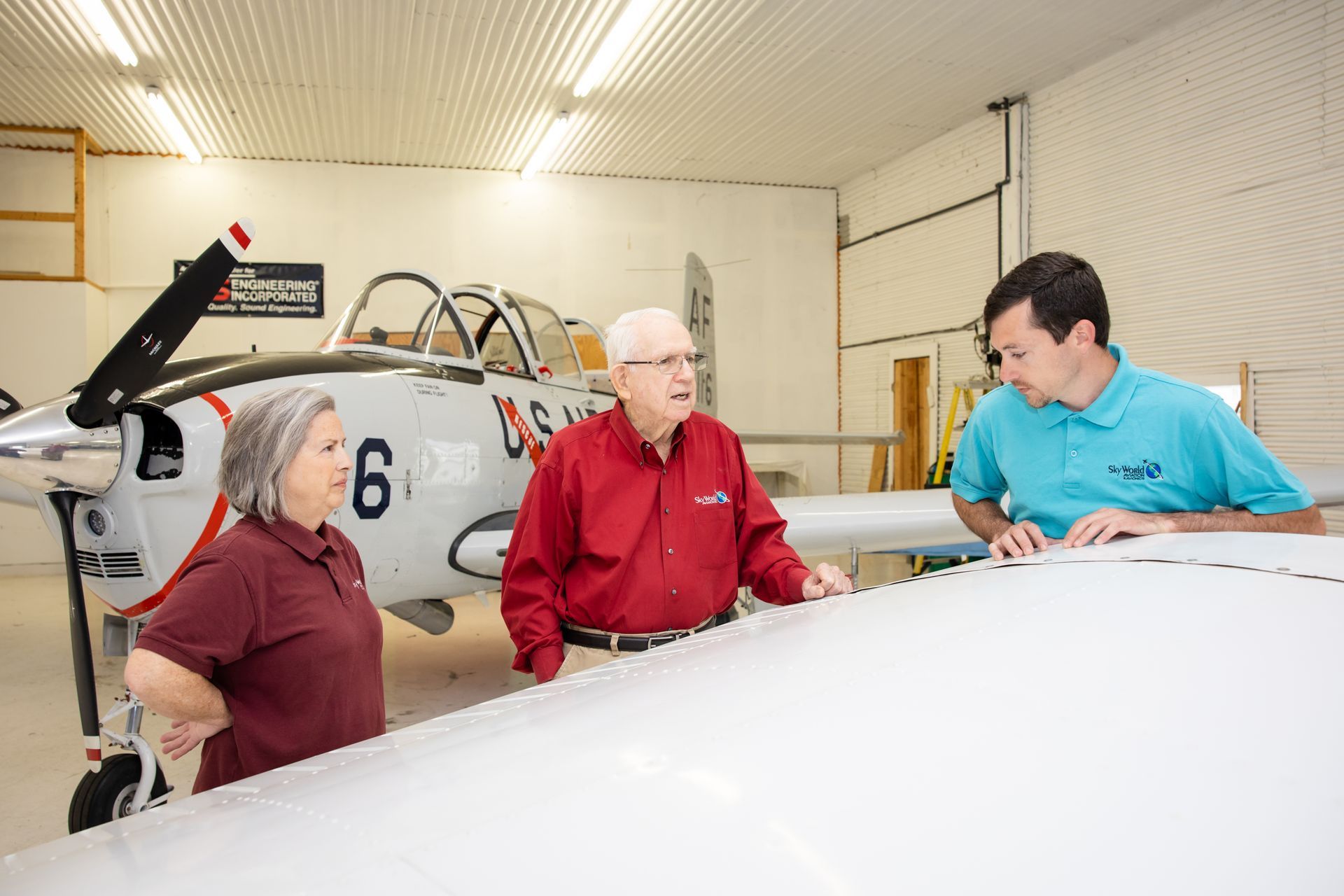 Three people talking beside a small airplane inside a hangar