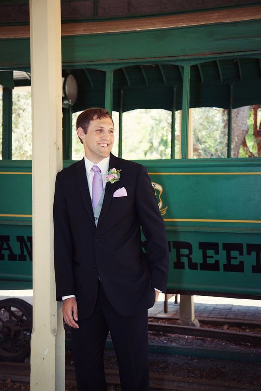 A man in a suit and tie is leaning against a pole in front of a green trolley that says reet on it