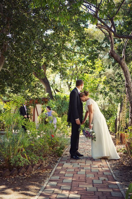 A bride and groom are kissing on a brick path in a garden.