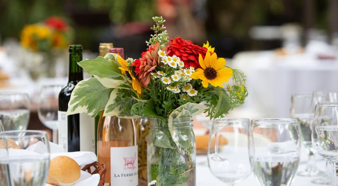 A vase filled with flowers and wine bottles on a table.