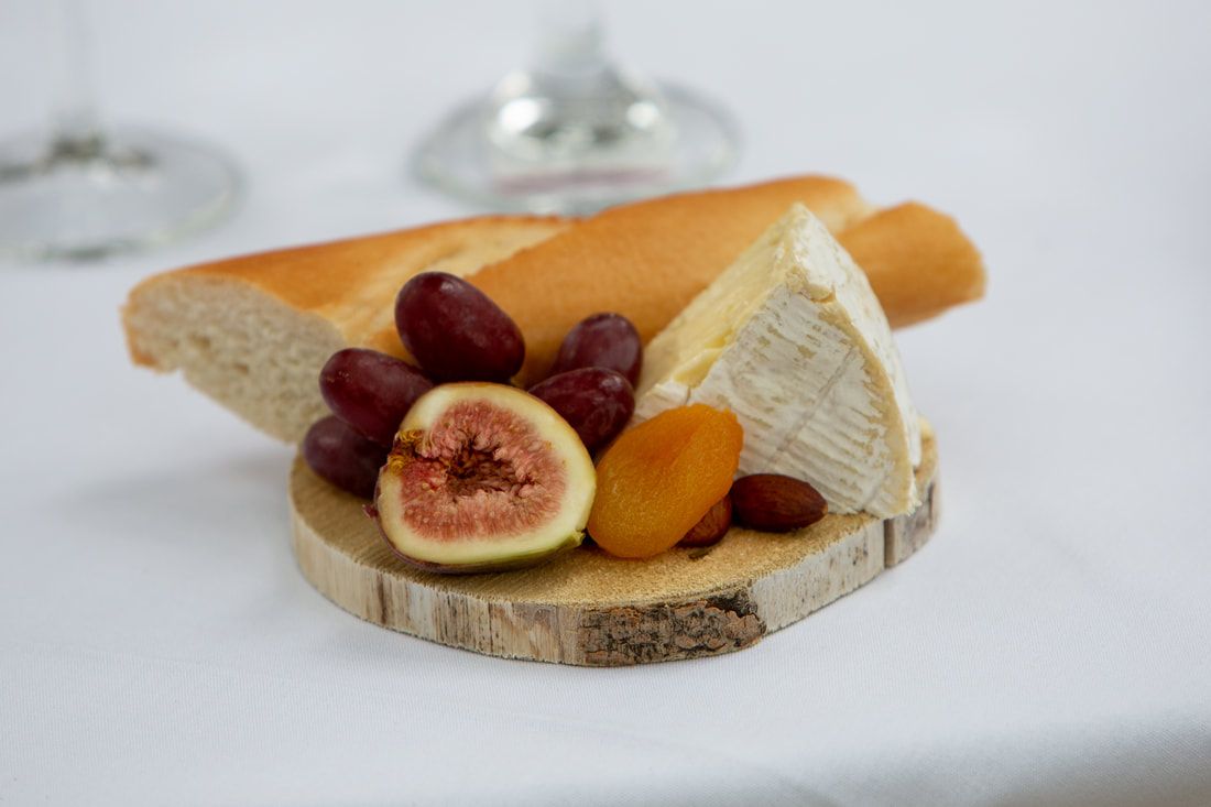 A wooden cutting board topped with cheese , grapes , figs and apricots.