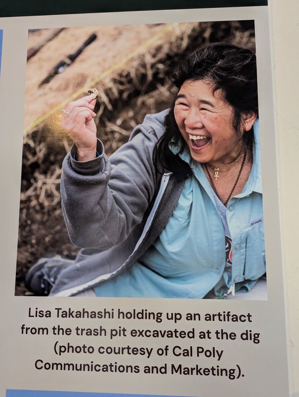 A woman is holding up an artifact from the trash pit excavated at the dig