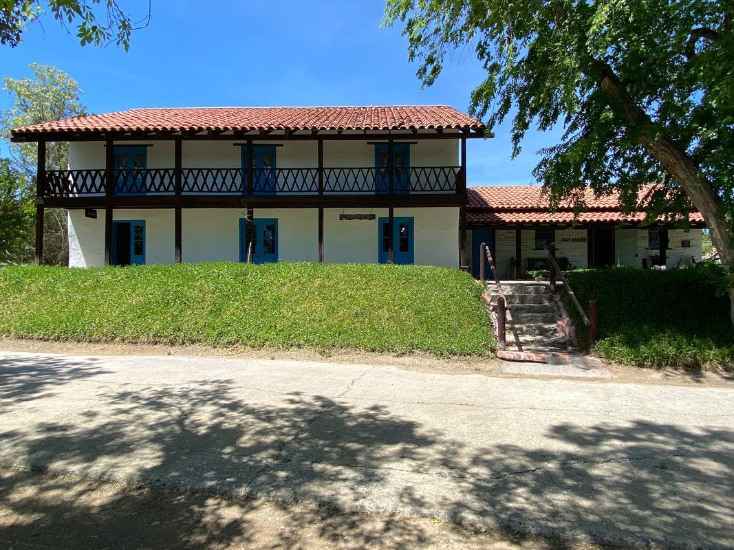 A large white house with a red tile roof is sitting on top of a grassy hill.