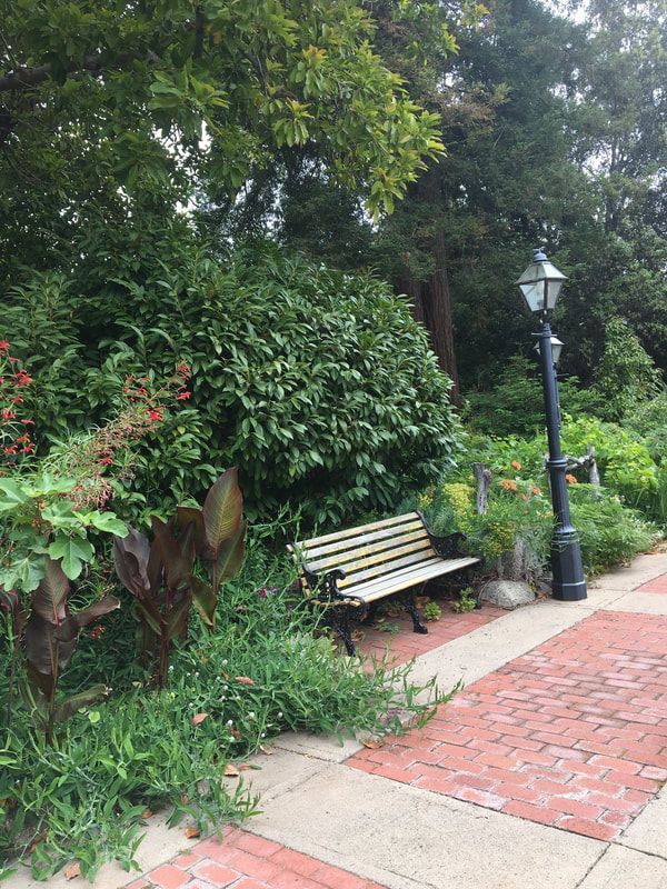 A park bench is sitting on a brick sidewalk next to a lamp post.