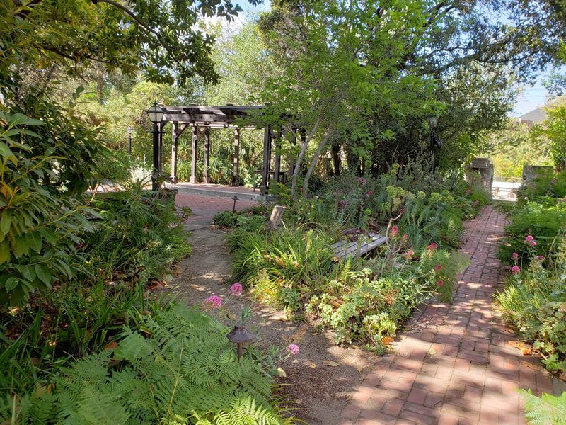 A brick walkway leading to a gazebo in a garden surrounded by trees and plants.