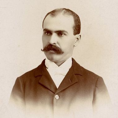 A man with a mustache is wearing a suit and bow tie