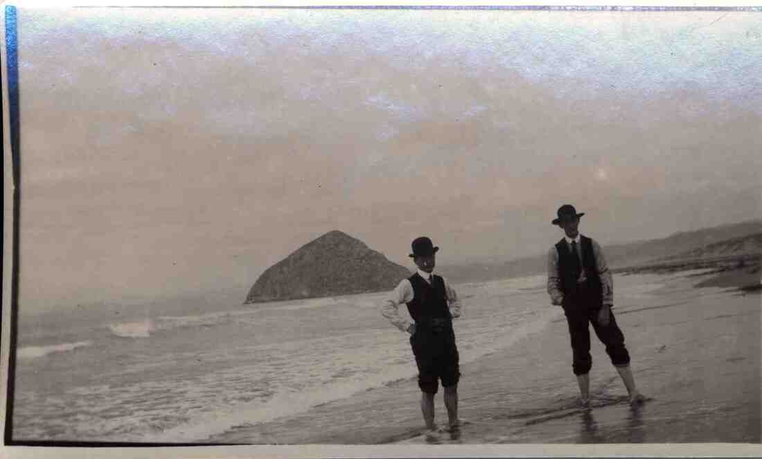 Two men are standing on a beach in a black and white photo.