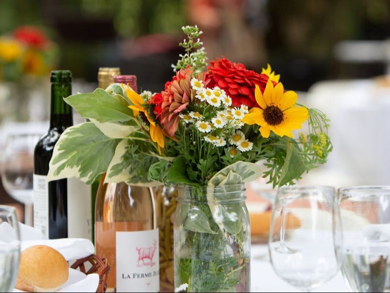 A vase of flowers sits on a table next to bottles of wine