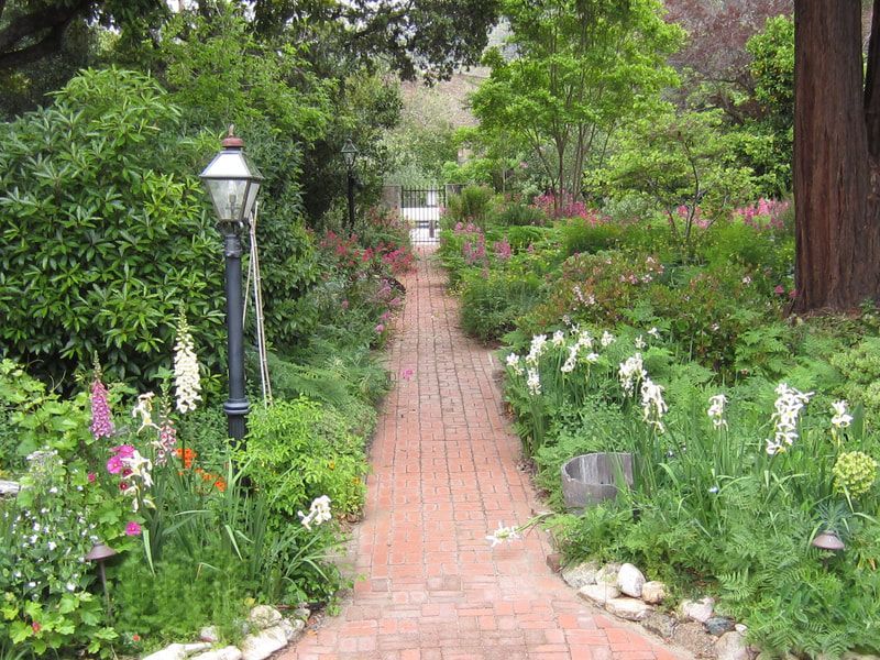 A brick walkway in a garden with flowers and trees