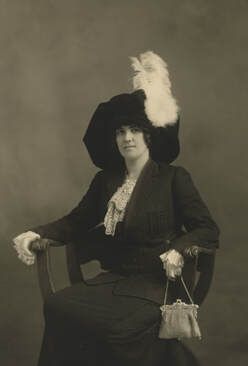 A woman is sitting in a chair wearing a hat and holding a purse.