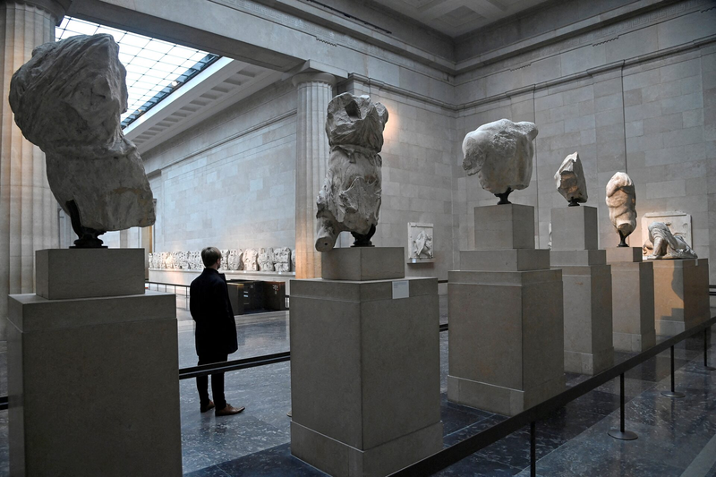 A man is standing in front of a row of statues in a museum.