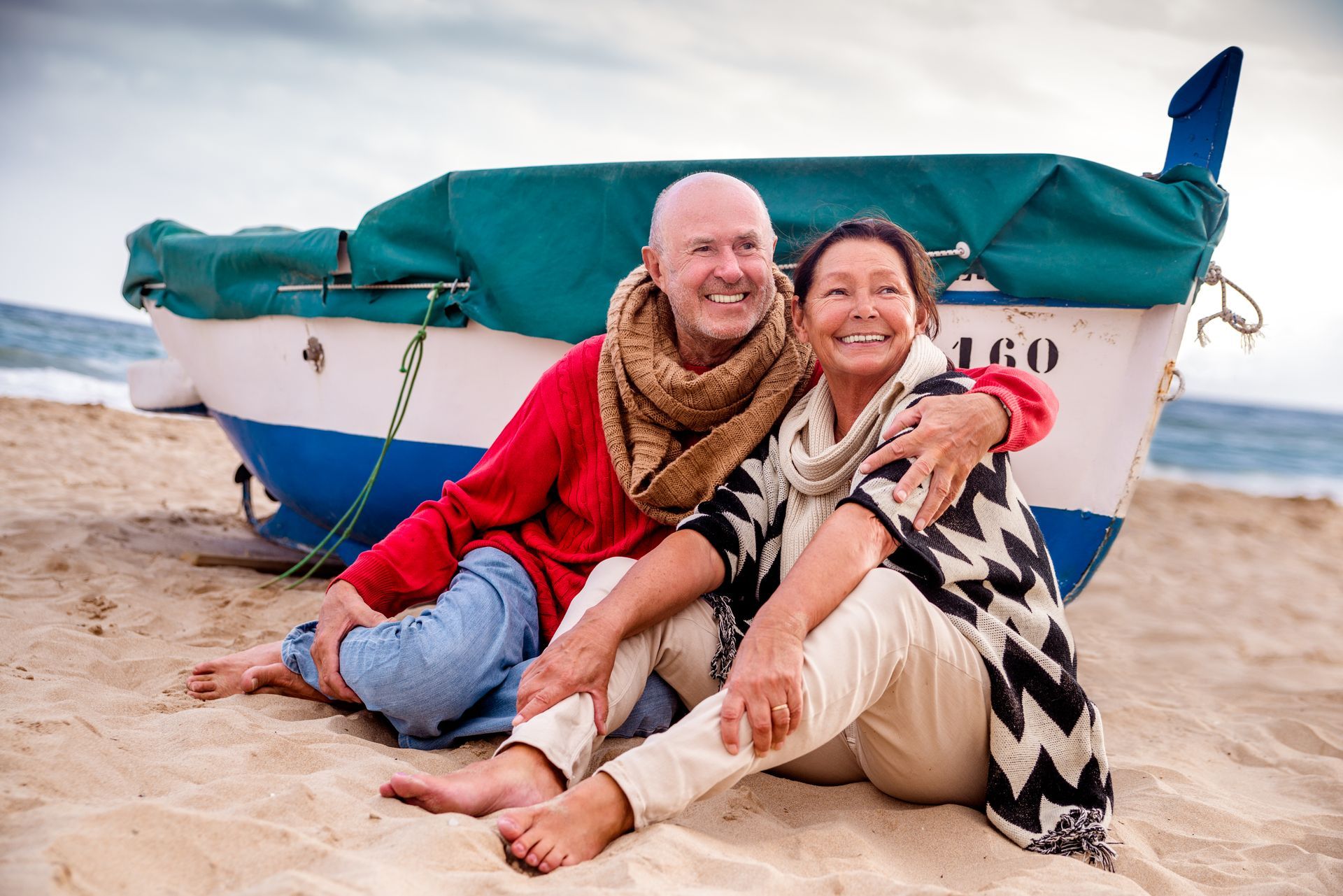 A man and a woman are sitting on the beach in front of a boat.